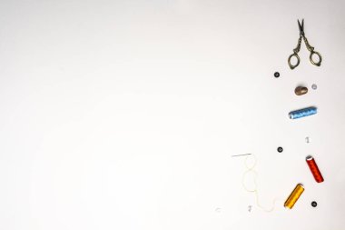 Spools of colored thread, with a threaded needle, gold scissors, and thimble on a white background