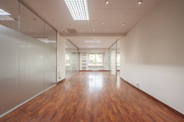 Several offices of an empty office with technical ceilings, windows to the street, glass partitions and reddish floating flooring