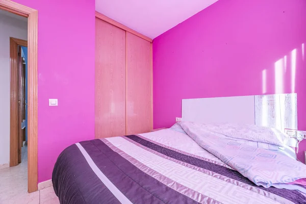 Bedroom with a double bed with a purple bedspread, pink walls and a built-in wardrobe with oak sliding doors
