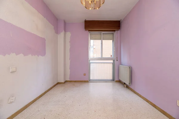 Empty bedroom with poorly painted pink walls, ceiling lamp, balcony and cream-toned terrazzo floors