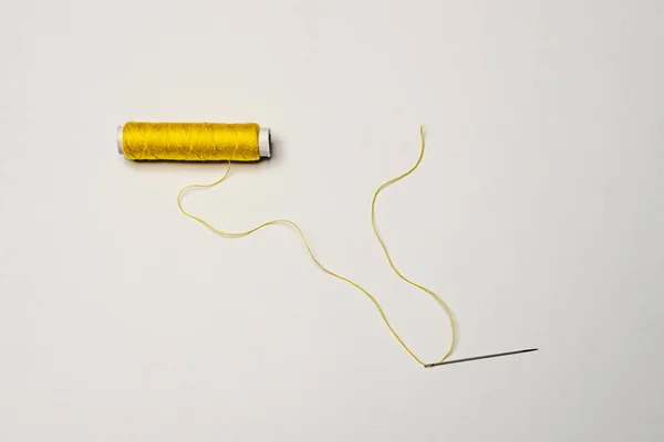Spool of yellow thread with a needle threaded with thread on a white background