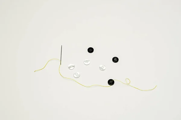 thread of yellow color with a threaded needle, black and white buttons along with the thread on a smooth white surface