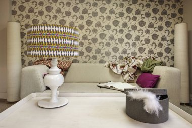 A space decorated with a patterned lamp on a white coffee table and in the background a sofa and a wall with patterned decorative paper