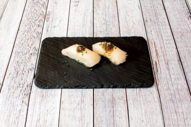 Some delicious lemon fish nigiris with chives with some sauce on a black slate