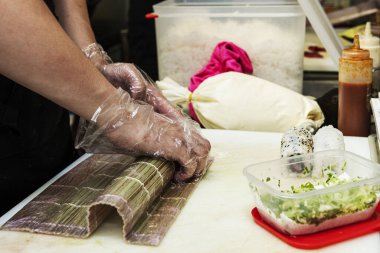 A chef with gloved hands making sushi rolls with Japanese rice, raw escado and vegetables