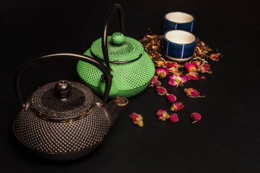 A couple of cast iron teapots along with some small porcelain cups and dried rose tea