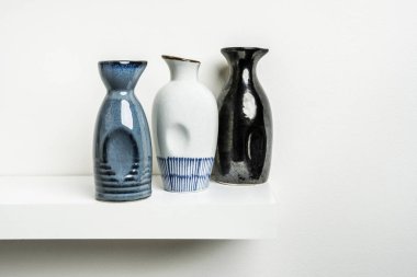 Small decorative porcelain bottles of different colors with drawings and grooves for a better hold placed on a white wooden shelf