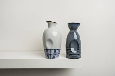 Beyaz rafta küçük beyaz ve mavi porselen şişeler var.