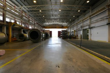 Çatı raylarında ağır vinçleri, büyük mekanik parçaları ve beton zemini olan bir fabrikanın deposu.