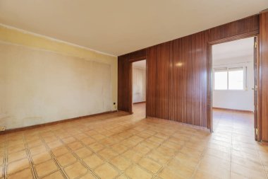 Ahşap duvarlarla kaplı bir oda, açık kapılı girişler ve açık kahverengi taş kaplama döşemeler.