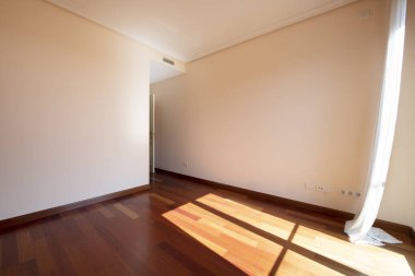 Kırmızımsı parke zeminli boş bir oda, pencereden süzülen bir güneş ışığı rüzgarda sallanan bir pencere.