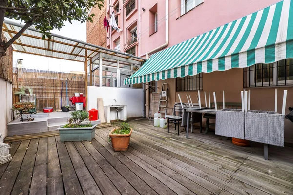 stock image Terrace patio of a house on the ground floor with some plants and unvarnished acacia wood floors, white and green two-tone awning and access porch