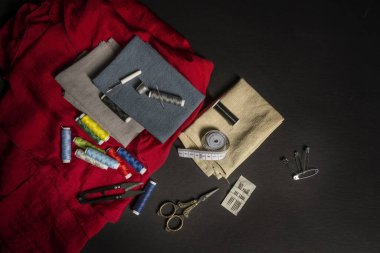 Klasik metal makas, çeşitli iğneler, renkli iplikler, kumaşlar, siyah arka planda şerit ölçüm aletleri olan bir takım dikiş aletleri.