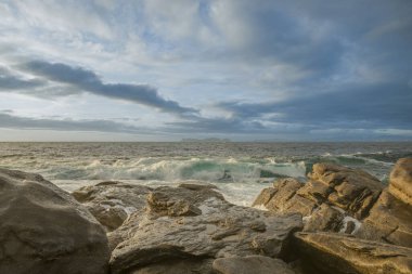 Dalgaların saldırısına uğrayan doğal dalgalar gün batımında ufuktaki bazı adaların görüntüleriyle bulutlarla dolu gökyüzü.