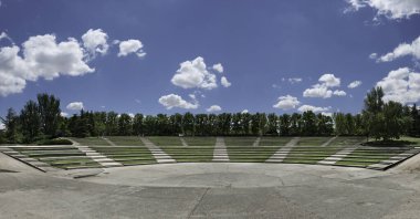 Geniş beton yüzeyi ve çimleri olan bir amfi tiyatronun panoramik görüntüsü.