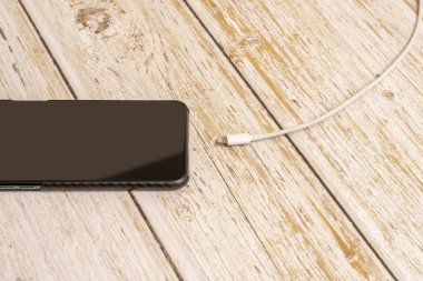 Karbon fiber çantalı telefon ve ahşap masadaki beyaz kablo bağlantısı kesilmiş.