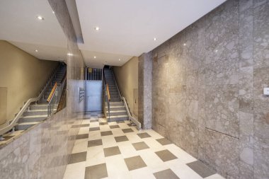 Mermer duvarları olan bir yerleşim yerinin kapısı, duvara entegre edilmiş büyük bir ayna ve asansörlü bir merdiven.