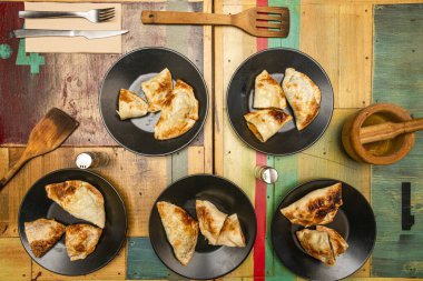 Dilimlenmiş böreklerle dolu siyah tabaklar renkli ahşap bir masada.