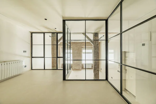 Loft-style room with glass partitions and black metal frame, plain beige walls and floors, and old wooden pillars