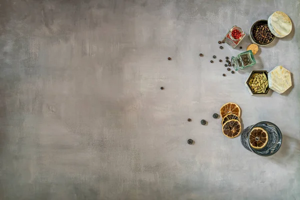 stock image A crystal glass with gin next to some jars with seasonings for preparing alcoholic cocktails on a gray-blue background