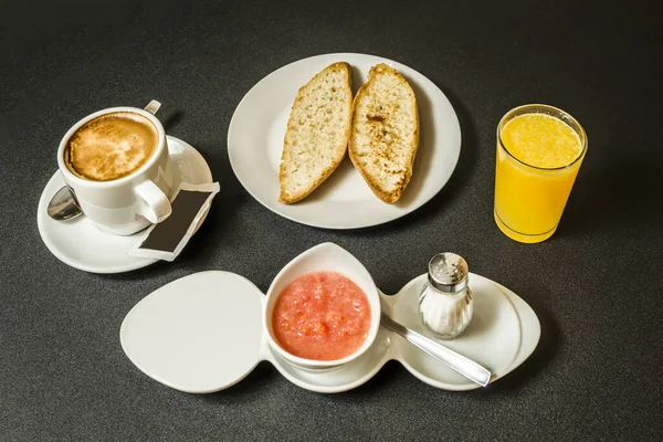 A Spanish breakfast with toasted bread with oil and tomato, coffee with milk and orange juice on a gray table