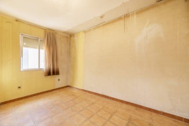 Kötü durumda bir dairede, duvarlarda iyi bir kat boya ve eski perdeli bir pencereye ihtiyacı olan bir oda.