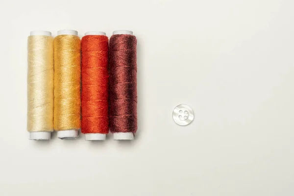 光沢のある白いボタンの横に 使用されていない黄色 日焼けや茶色の柔らかい色合いで糸を縫うのブランドの新しいスプール — ストック写真