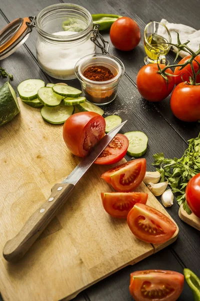 Stock image Some ripe split tomatoes together with garlic, cucumber slices, paprika, olive oil and a knife on a table