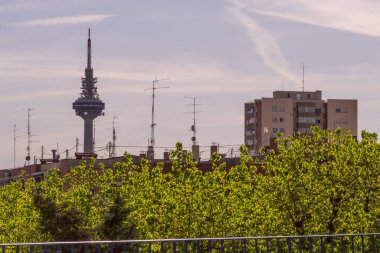 Madrid şehrinin haberleşme kulesinin yakınındaki binaların cepheleri, ağaçları ve çatıları.