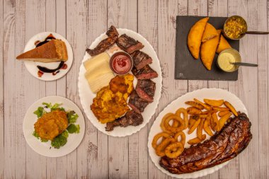 En çok parsera yapan Kolombiya mutfağından, kömür etleriyle, acı soslu mısır böreğiyle, bir porsiyon quesillo ve beyaz ahşap bir masada doldurulmuş patates karışımı.