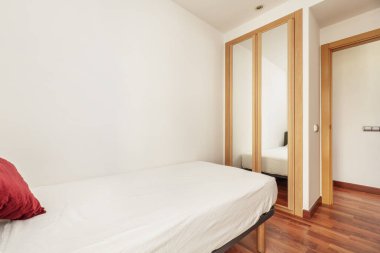 Yatak örtüsü olmayan küçük bir yatak odası ve aynalarla kaplı sürgülü kapıları olan bir gardırop.