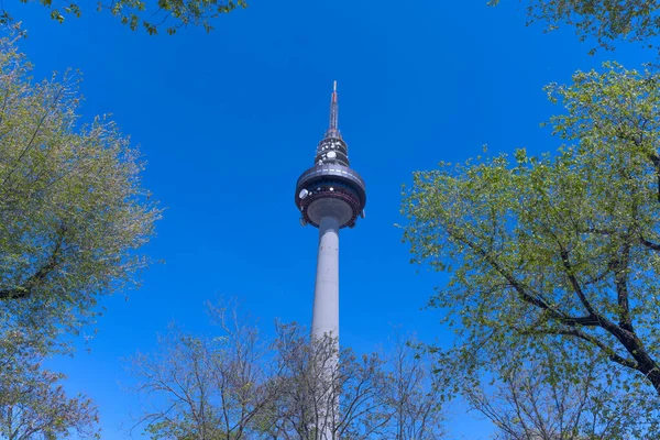 stock image Telecommunications tower in Madrid together with a frame of tree branches with leaves and a bit of blue sky