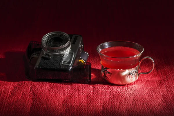 Some old cameras with a roll of film in a reddish environment with a glass of forest fruit roibos