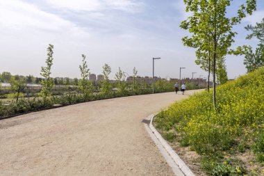 Emekli çift yeni bir şehir parkında kumlu kaldırımda geziniyor ve bir sürü çiçek.