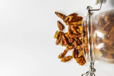 Kurutulmuş arnavut biberiyle dolu cam bir kavanoz pürüzsüz beyaz bir yüzeye devrildi.