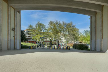 Bir şehir köprüsünün dibinde oyun parkı ve yerde bir sürü kum var.