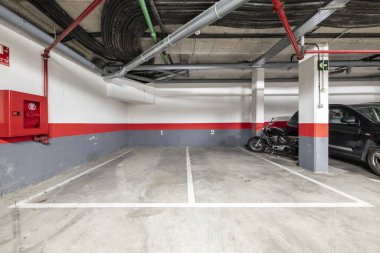 Kırmızı, gri boya ve beton zemini olan bir apartmanın bodrumunda birkaç boş park yeri.