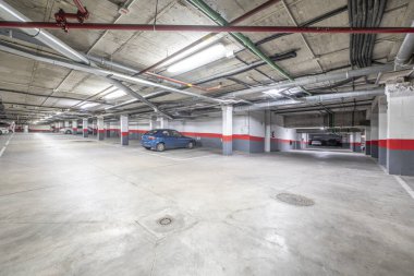 Beyaz ve kırmızı sütunları ve sınırları olan bir apartmandaki büyük bir garajın birkaç park yeri.