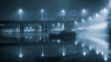 Işıkları açık ve sisli bir nehri kurtaran bir köprünün gece görüntüsü