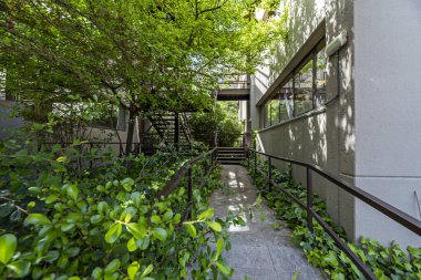 Bitkileri, ağaçları, çiçekleri ve kahverengi metal parmaklıkları olan bir binanın iç avlusu.