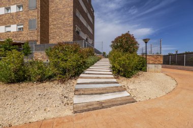 Yeni bir binanın girişine giden çitler arasında tahta ve beton bir yol.