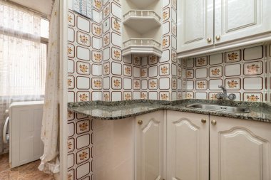 Granit tezgahlar, eski kare fayanslar, beyaz dolaplar ve çamaşır makinesi ile donatılmış bir mutfak.