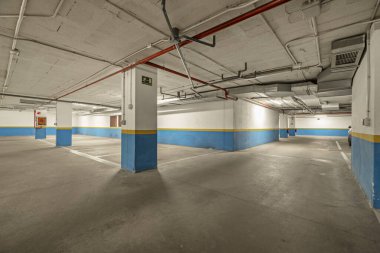 Yarı mavi, yarı beyaz beton duvarları ve kirli beton zemini olan bir apartmanın park yeri.