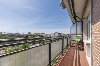 Metal parmaklıklı, şeffaf camlı ve şehir manzaralı bir evin dar terası.