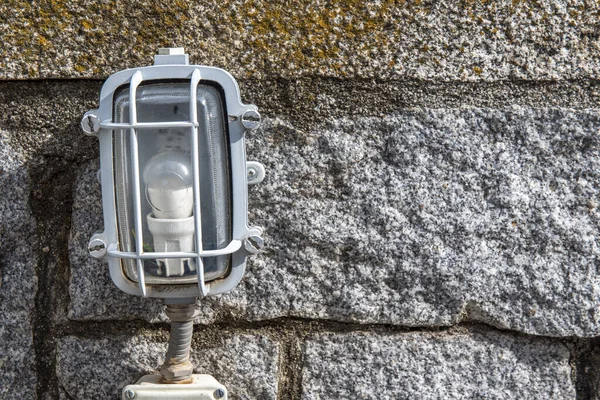 An outdoor lamp with a grill attached to a stone wall