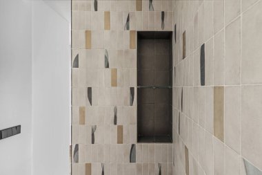 Modern bir banyodaki duş kabininin duvarında cam bir raf var.