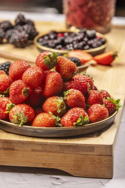 Bir tepsi küçük olgun çilek ve arkasında daha fazla dut