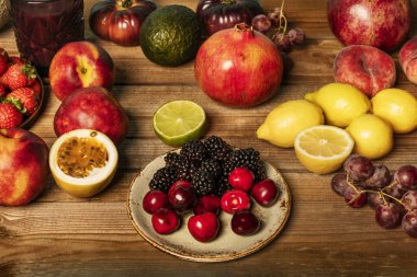 Olgun kirazlar, çekirdeksiz üzümler, limonlar, limonlar ve verniksiz ahşap bir masada böğürtlenlerle dolu sakin bir hayat.