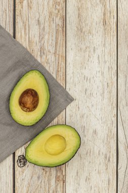 Gri bir kumaş ve açık renkli ahşap bir masa üzerinde ikiye bölünmüş olgun bir avokado.