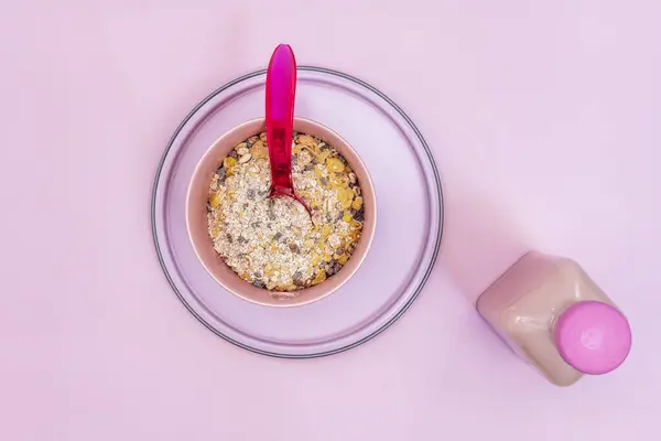 A still life of cereals in a pink bowl with a pink spoon on a plate and a background of the same color